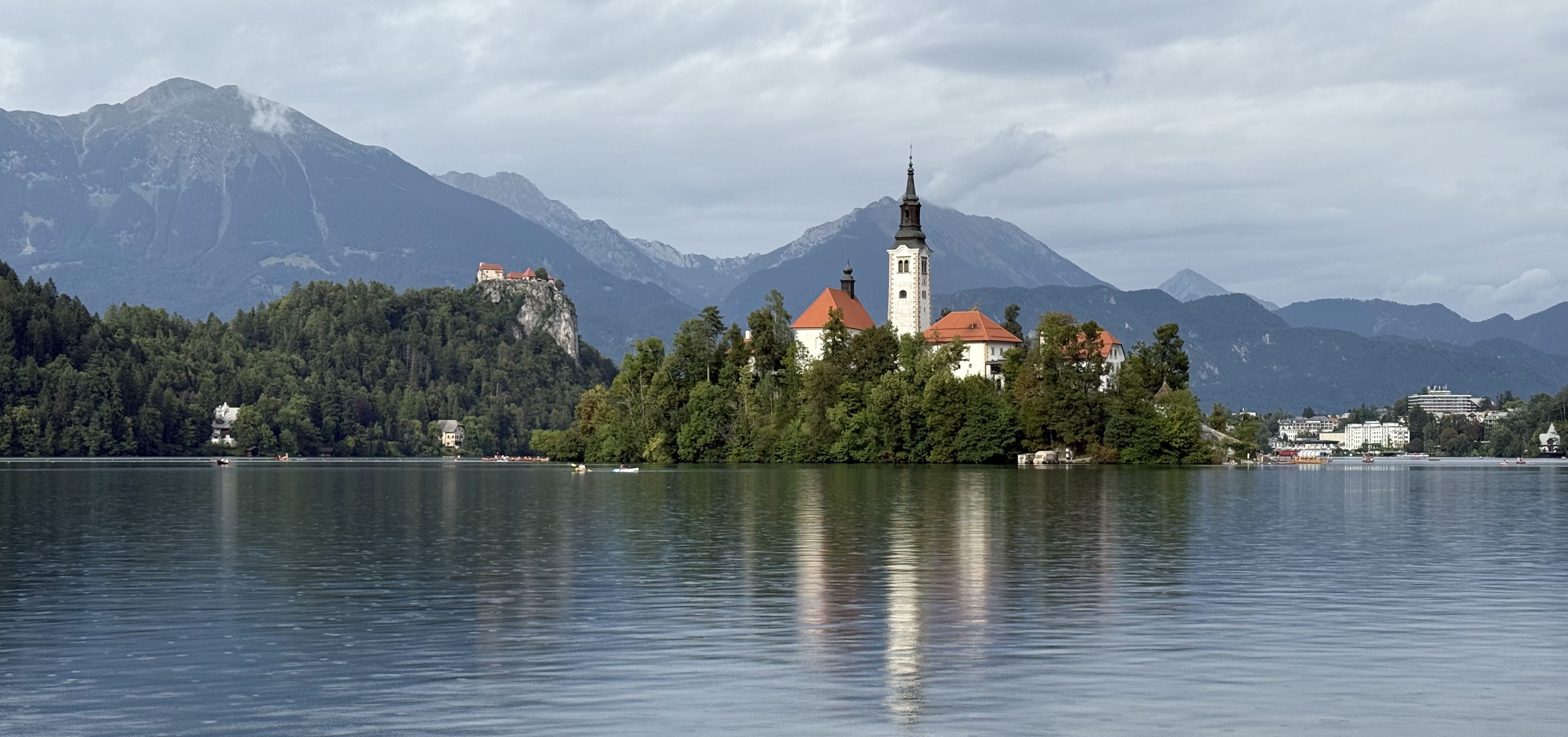 Vista del lago Bled con la isla y la iglesia en el centro, rodeada de montañas y vegetación.